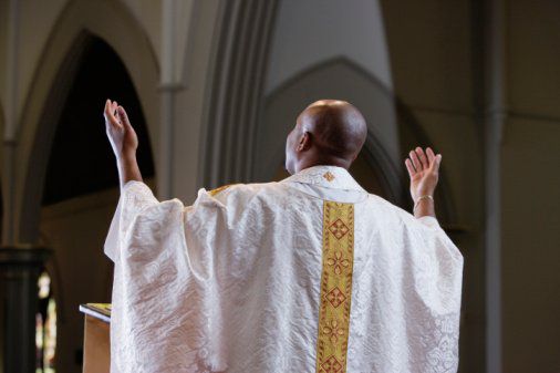 Priest praying in church, rear view
