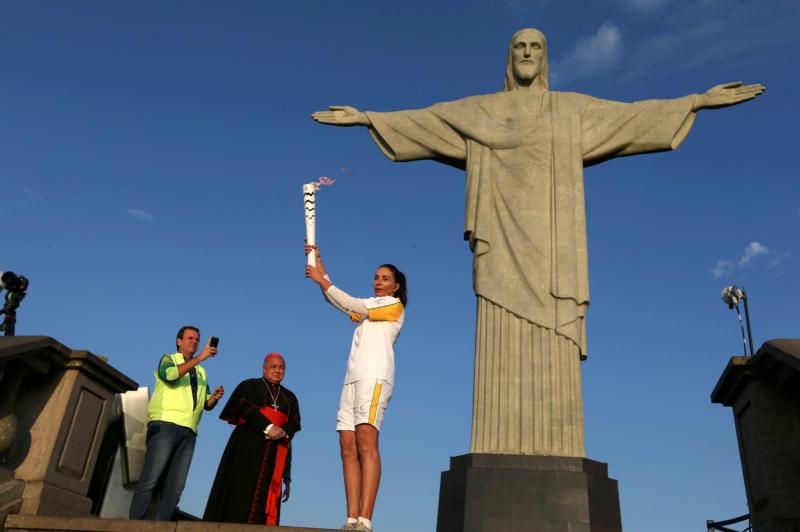 Former Brazilian volleyball player Isabel Barroso holds the Olympic torch Aug. 5 next to the Christ the Redeemer statue as Rio de Janeiro Mayor Eduardo Paes and Cardinal Orani Tempesta look on. (CNS photo/Pilar Olivares, Reuters) See OLYMPICS-TORCH-STATUE Aug. 5, 2016.
